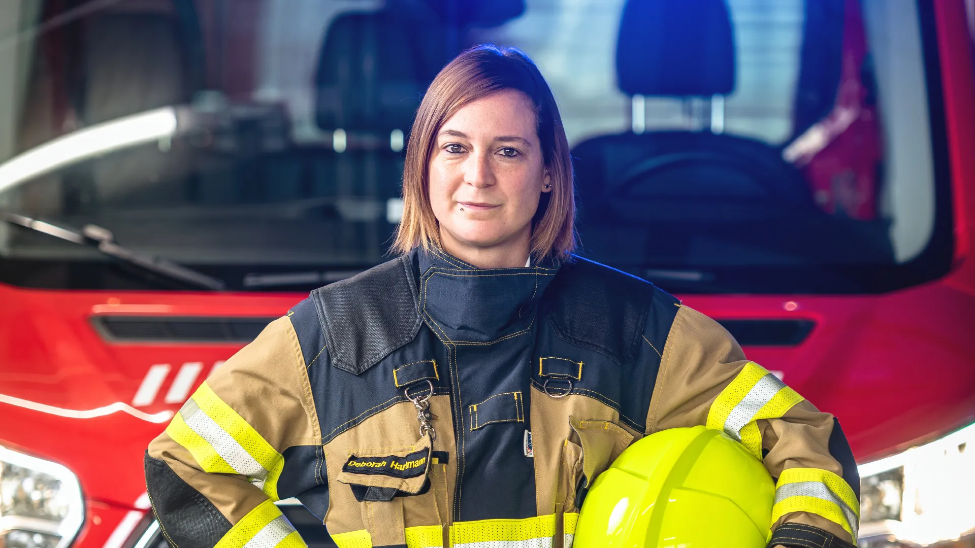 Eine Mitarbeiterin der Feuerwehr steht vor einem Feuerwehrauto.