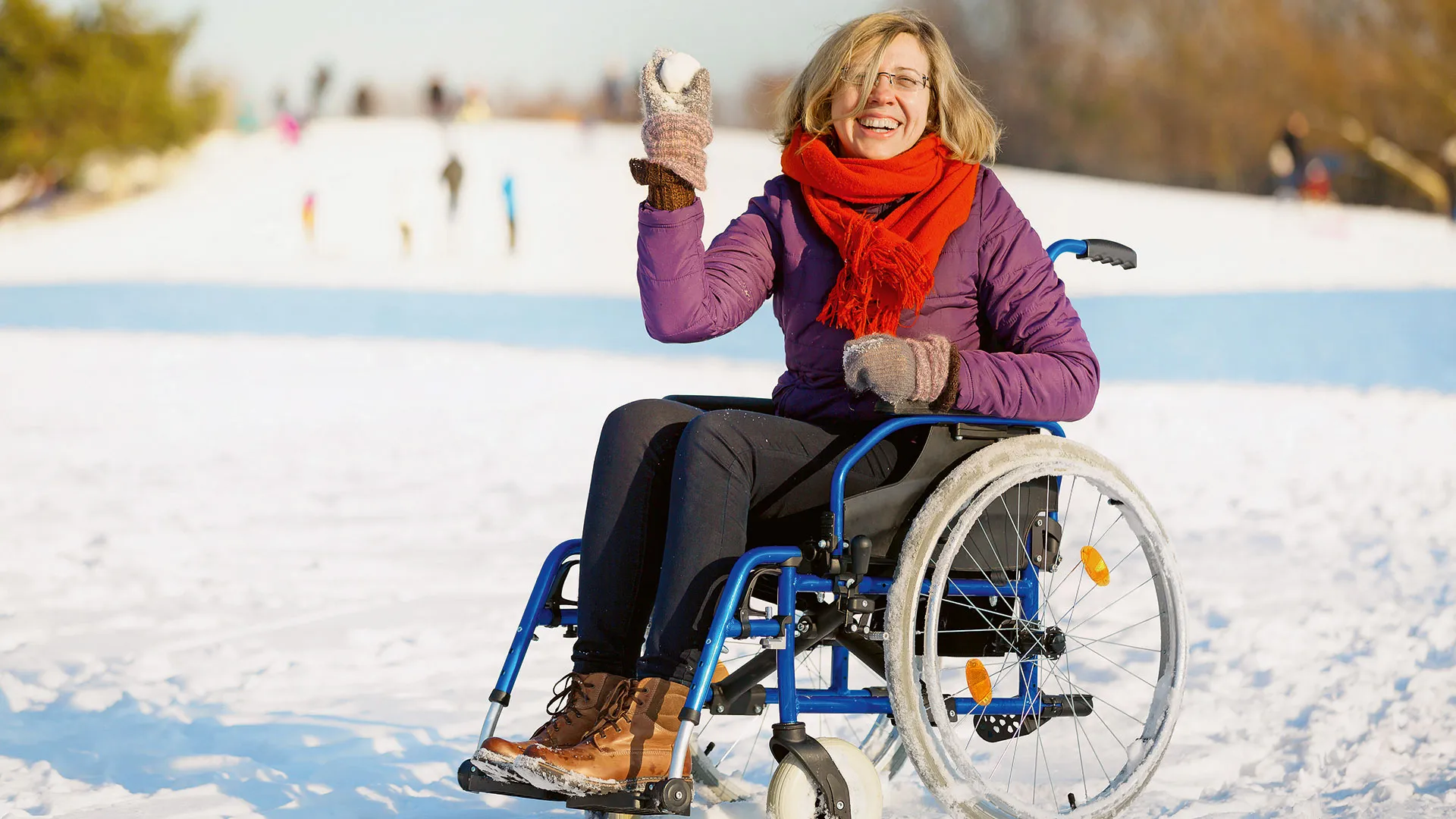 Lachende Frau sitzt im Rollstuhl und wirft einen Schneeball