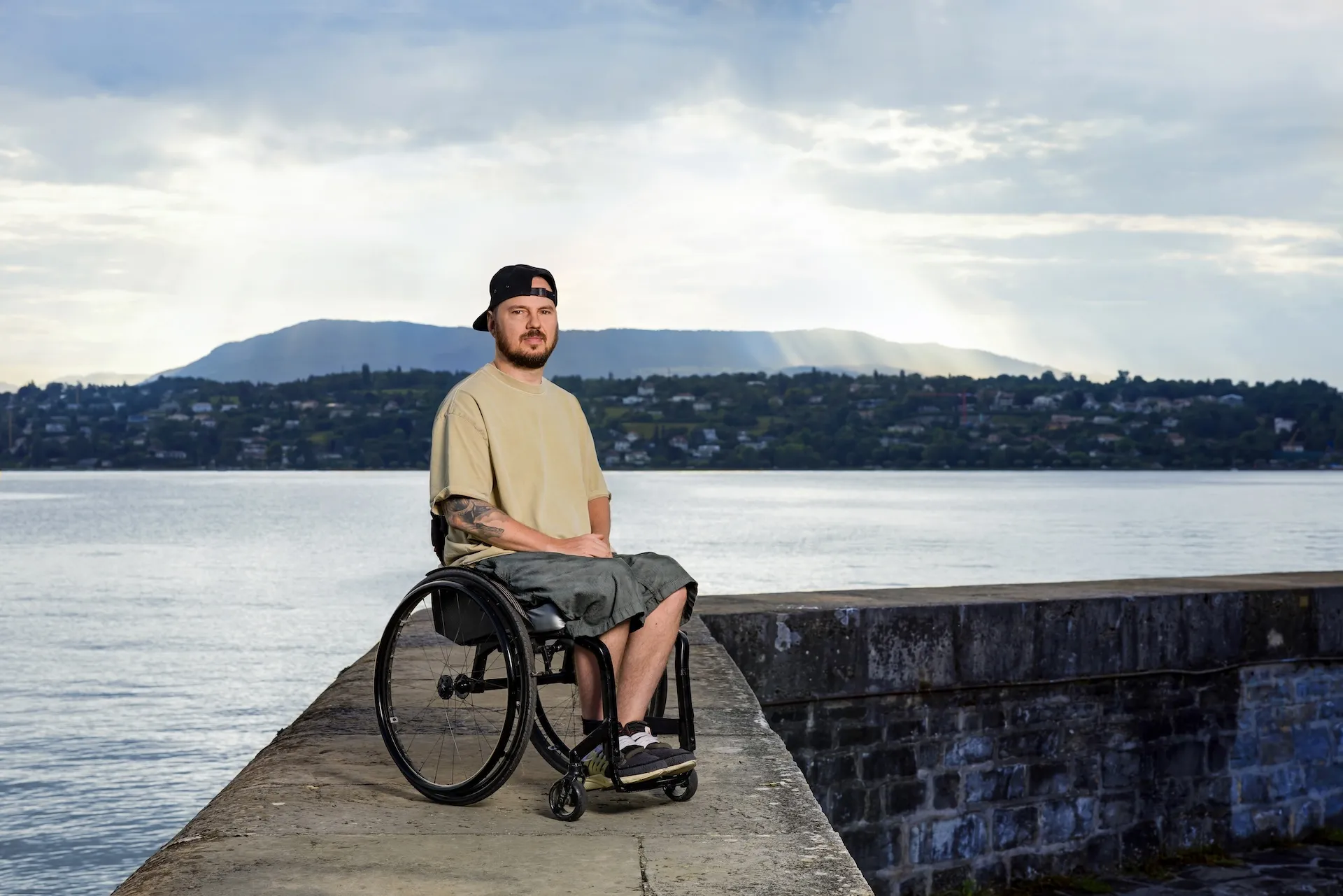 Anton Mityukov sitzt im Rollstuhl auf einem Steg aus Beton mit dem Genfersee im Hintergrund.