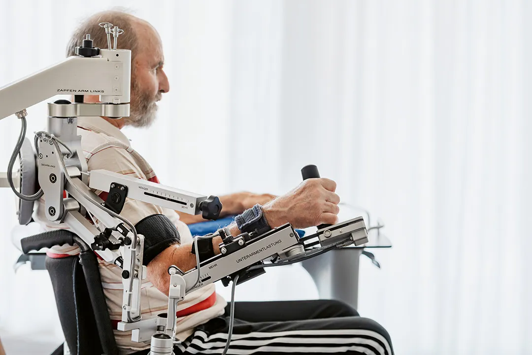 Ein Mann sitzt in einem Stuhl und übt mit einer Roboterhand.