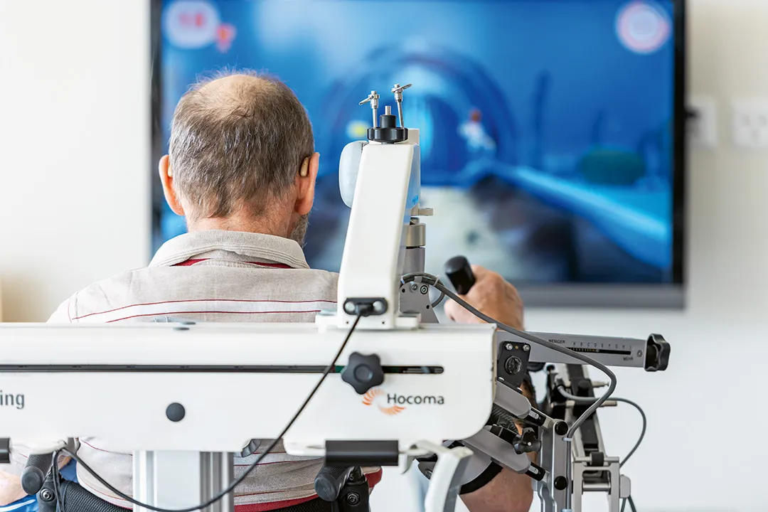 Ein Mann sitzt vor einem Bildschirm und übt mit einer Roboterhand.